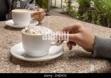 Teilen einer Tasse Kaffee mit Creme in einem Restaurant, Details der Hände, die das Geschirr und den Tisch halten, Lifestyle und Getränk zum Frühstück Stockfoto