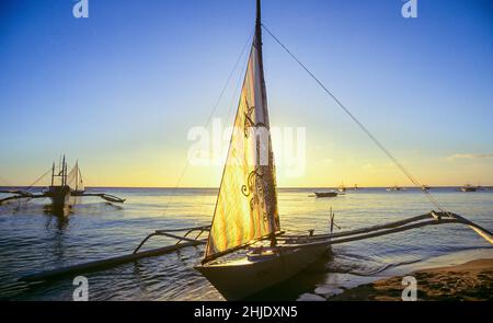 Ein Auslegerboot liegt am White Beach auf der Insel Boracay in der Region Western Visayas auf den Philippinen. Boracay ist heute ein wichtiger Tourismusauszug auf den Philippinen und wurde von Reisezeitschriften und Organisationen der Tourismusbranche immer wieder zu einem der besten Strandtourismus-Standorte der Welt gewählt. Stockfoto