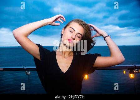 Die junge ukrainische Dame genießt ihre Zeit in einem Nachtclub in Odessa am Schwarzen Meer in romantischer Stimmung. Ein dramatischer Himmel sorgt für einen Kontrast zu ihrem Bild. Stockfoto