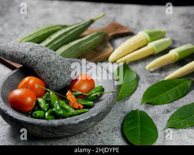 Chilies und Tomaten im Mörser, Rezept für Gemüsekorn und Luffa acutangula mit Tomatensauce. Konzept zur Zubereitung von Speisen. Stockfoto