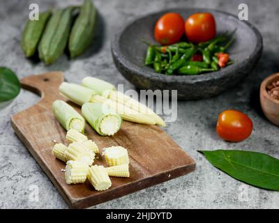 Geschnittener Babykorn auf einem hölzernen Schneidebrett. cayennepfeffer und Tomaten im Mörser. Food Rezept Konzept. Stockfoto