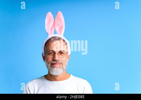 Niedlicher reifer Mann mit Hasenohren bereit zum osterfest auf blauem Hintergrund Stockfoto