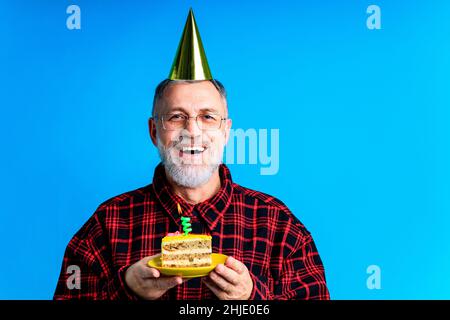 Mann trägt Geburtstagshut mit Kuchen isoliert auf hellblauen Hintergrund, Studio-Porträt Stockfoto