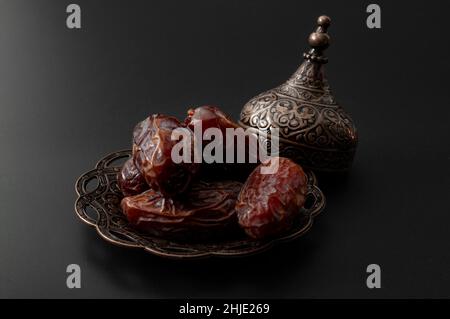 Ramadan-Süßigkeiten und Trockenobst-Konzept aus dem Nahen Osten mit Nahaufnahme von trockenen Datteln auf wunderschön verzierten Metallplatten isoliert auf schwarzem Backgr Stockfoto