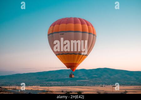 Malerische Aussicht auf einen orangefarbenen Heißluftballon am blauen Himmel gegen Berge Stockfoto