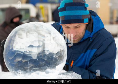 Ein Bildhauer schnitzt mit einem Meißel eine runde Eiskugel aus einem Eisblock. Stockfoto