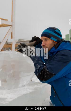 Ein Bildhauer schnitzt mit einem Meißel eine runde Eiskugel aus einem Eisblock. Stockfoto