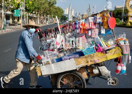 Ein mobiler Verkäufer eilt, um seinen Wagen über die Rajdamnoen Klang Avenue in Bangkok, Thailand, zu schieben; im Hintergrund gesehen: Das Demokratiedenkmal Stockfoto