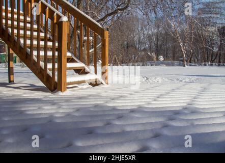 Im Winter mit natürlichem Sonnenlicht bietet sich auf einer Holzterrasse und einer Treppe ein Blick im Freien auf frische Schneedesigns Stockfoto