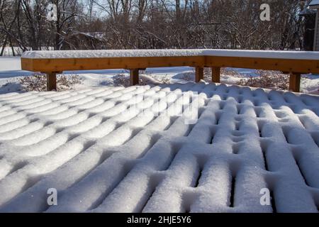 Im Winter mit natürlichem Sonnenlicht können Sie auf einer Holzterrasse und -Bank frische Schneedesigns im Freien betrachten Stockfoto