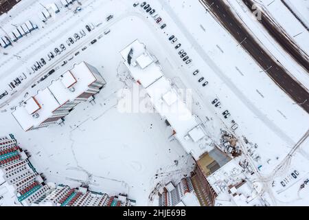 Luftaufnahme des Hofes eines Hochhauses. Schneebedeckte Autos und Straßen in der Winterstadt. Stockfoto