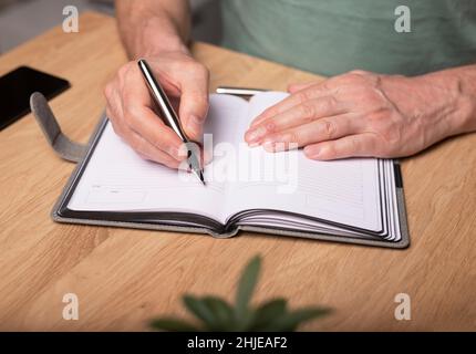 Männliche Hände machen Notizen, schreiben Pläne in Notizbuch oder Planer. Planung im Terminkalender, Nahaufnahme. Stockfoto