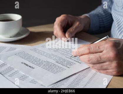 Mann, der den Vertrag liest, um ihn am Schreibtisch zu unterschreiben. Stockfoto