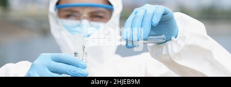 Wissenschaftler im Schutzanzug mit Gläsern gießt Wasser aus dem Reagenzglas in den Kolben Stockfoto