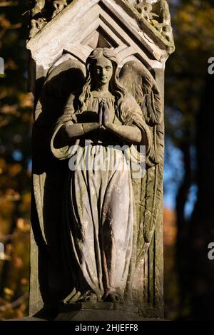 Engel mit betenden Händen und herzliches Lächeln, alte Steinskulptur aus Friedhofsgrabstein, geflügelte Frauenfigur im Gebet und Segen für die Toten. Stockfoto