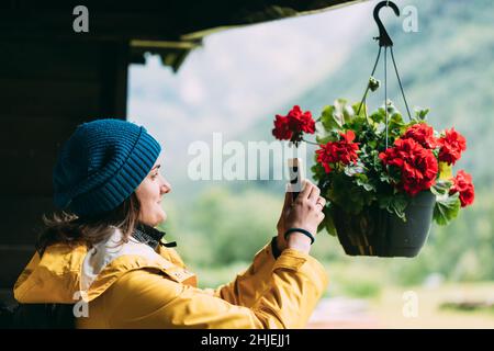 Junge Dame der Touristeninformation fotografiert EINEN hängenden Blumentopf am Telefon Stockfoto