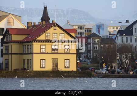 Der Blick über den Tjörnin-See in Reykjavik, Island, im Januar mit einem ikonischen gelben Gebäude am fernen Ufer Stockfoto