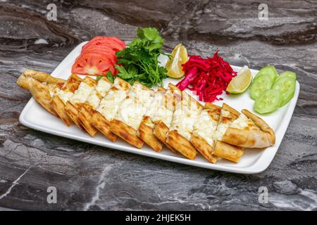 Türkischer Pide oder Pita mit Cheddar-Käse und Halloumi-Käse mit Salat und Beilagen auf einem weißen Teller Stockfoto