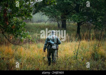 Einzeldarsteller als deutscher Wehrmachtsinfanteriesoldat im Zweiten Weltkrieg bei einem Spaziergang in Patrol durch den Herbstwald. WW2-mal im Zweiten Weltkrieg Stockfoto