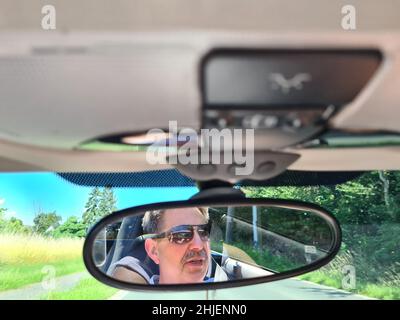 Spiegelung der seniorenaugen im Rückspiegel des Autos Mit nasser Windschutzscheibe Stockfoto