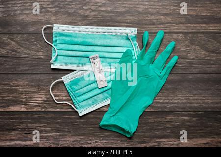 Coronavirus-Test (COVID-19) und Gesichtsmasken auf Holzhintergrund, schneller Antigen-Selbsttest zeigt positive Ergebnisse für SARS-CoV-2-Virus. Stockfoto