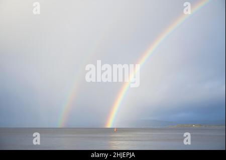 Heller Regenbogen hoch im Himmel über dem Meer während des dunklen Sturms Stockfoto