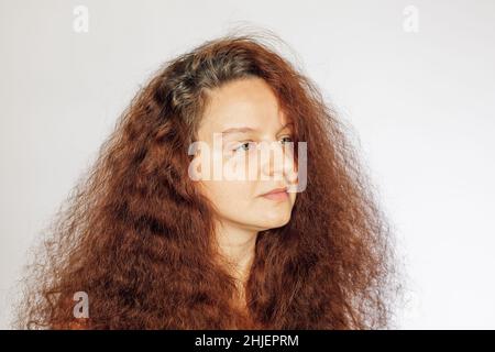 Kaukasische junge Frau mit rot gefärbten üppigen welligen Haaren, weicher und sauberer Gesichtshaut ohne Make-up mit Augen, die auf weißem Hintergrund wegschauen. Selbst Stockfoto