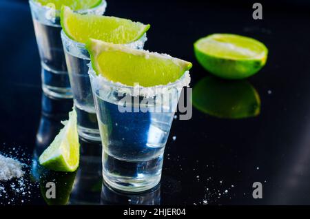 Silberner Tequila mit Kalk und Salz auf einem schwarzen Tisch Stockfoto