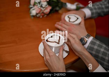 Kaffeetassen Herz Latte Kunst, in den Händen eines Mannes und einer Frau. Selektive Fokussierung. Stockfoto