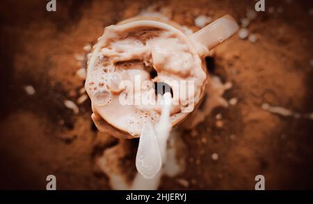Der Mensch goss schlampig Milch in einen Becher mit warmem Kakao. Chaos in der Küche. Ein erfrischendes Getränk zum Frühstück. Kaffee mit Milch. Stockfoto