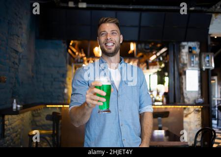 Schöner Mann, der zum St. Patrick's Day ein Bier in einer Kneipe hält Stockfoto