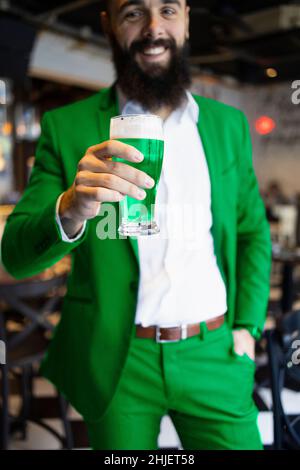 Bärtiger Mann, der zum St. Patrick's Day in Grün gekleidet war und ein Bier hielt Stockfoto