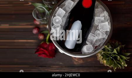 Flasche Champagner in einem Eimer mit Eis, Rose, Ananas und Gläsern, auf einem hölzernen Hintergrund mit Platz für Text Stockfoto