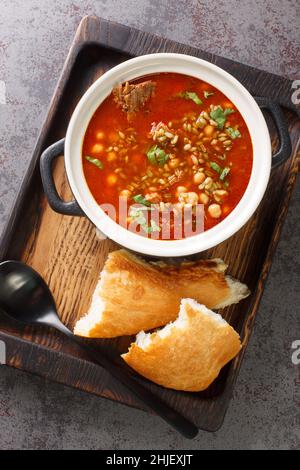 Chorba Hamra bel Frik algerisches Lamm, Tomate und Freekeh-Suppe in Nahaufnahme auf einem Teller auf dem Tisch. Vertikale Draufsicht von oben Stockfoto