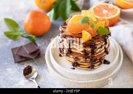 Wir feiern den Pfannkuchen-Tag, ein gesundes Frühstück. Köstliche hausgemachte pfannkuchen mit amerikanischen Bananen mit Schokolade und roter Orange auf grauem Steingrund. Stockfoto