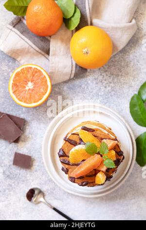Wir feiern den Pfannkuchen-Tag, ein gesundes Frühstück. Köstliche hausgemachte pfannkuchen mit amerikanischen Bananen mit Schokolade und roter Orange auf grauem Steingrund. Flach Stockfoto