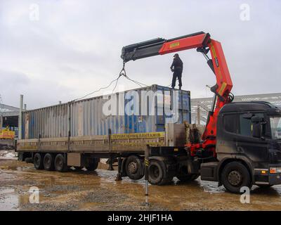 Kiew, Ukraine. Januar 14. 2011. Ein Manipulator-LKW lädt mit Hilfe eines Krans einen schmutzigen blauen Container. Es ist ein Mann auf dem Container. Stockfoto