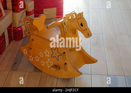 Schaukelpferd für Kinder aus Holz, Weihnachtsszene, Geschenke unter dem Neujahrsbaum, weiche Hintergrundbeleuchtung. Stockfoto