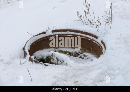 Offener Kanalkanal mit im Winter schneebedecktem Müll. Gefährliche Notwasserkanäle. Stockfoto