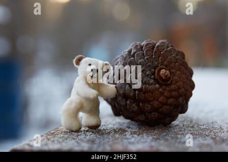 Handgenäht Mikro-Plüsch Teddybär rollt einen großen Tannenzapfen. Copy Space Stockfoto