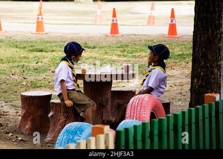 Thai Kinder Student junge Scout und Freund Pause sitzen entspannen Sie sich auf Stein Stuhl im Garten Park der Grundschule in Si Prachan Landschaft bei Suphanburi Stockfoto