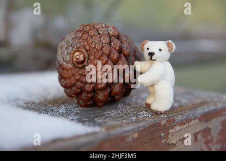 Handgenähter, mikroplüschiger Teddybär rollt einen großen Tannenzapfen Stockfoto