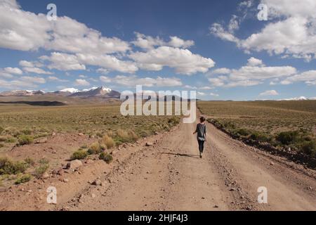 Frauen, die in Bolivien auf einer endlosen Bergstraße spazieren. Anden-Hochebene auf mehr als 4500 Meter über dem Meeresspiegel Stockfoto