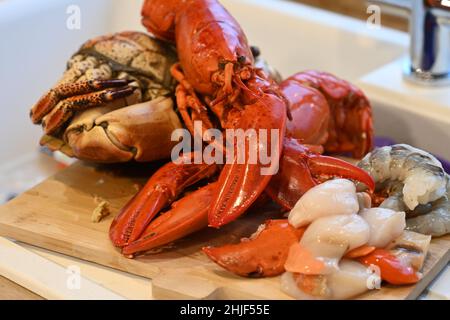 Krebs-Pagurus gekochte Krabben, kanadischer Hummer, frische rohe Jakobsmuscheln und frische rohe Garnelen, die auf einem hölzernen Küchentafel liegen Stockfoto