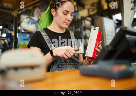 Crop junge Frau mit langen hellen Dreadlocks Scannen Barcode beim Kauf an der Theke im Einzelhandel Stockfoto