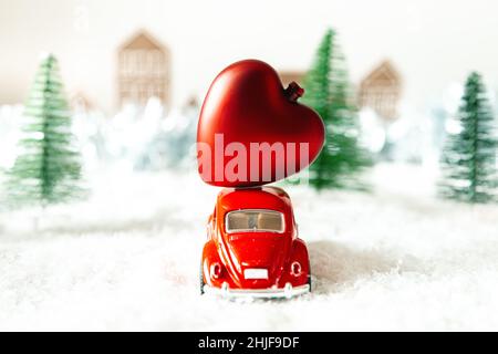 Rotes Retro-Auto mit Herz in einer Winterlandschaft. Postkarte zum Valentinstag. Urlaubslieferung. Selektiver Fokus. Stockfoto