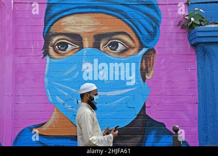 Mumbai, Indien. 29th Januar 2022. Ein muslimischer Mann, der eine schützende Gesichtsmaske trägt, überprüft sein Telefon, während er in Mumbai an einem Graffiti vorbeigeht.Coronavirus-Graffiti werden gemalt, um Bewusstsein zu schaffen und die Botschaft über die Aufrechterhaltung sozialer Distanz, das Tragen von Gesichtsmasken und die regelmäßige Desinfektion zu verbreiten. Kredit: SOPA Images Limited/Alamy Live Nachrichten Stockfoto