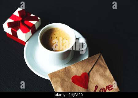 Tasse Espresso mit Geschenk und valentinstag. Schwarzer Hintergrund, selektiver Fokus. Stockfoto
