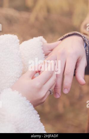 Die Braut legt den Ring auf den Finger des Bräutigams. Winterabend, draußen. Selektiver Fokus. Stockfoto