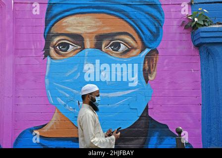 Mumbai, Indien. 29th Januar 2022. Ein muslimischer Mann, der eine schützende Gesichtsmaske trägt, überprüft sein Telefon, während er in Mumbai an einem Graffiti vorbeigeht.Coronavirus-Graffiti werden gemalt, um Bewusstsein zu schaffen und die Botschaft über die Aufrechterhaltung sozialer Distanz, das Tragen von Gesichtsmasken und die regelmäßige Desinfektion zu verbreiten. (Foto von Ashish Vaishnav/SOPA Images/Sipa USA) Quelle: SIPA USA/Alamy Live News Stockfoto